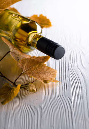 An unopened bottle of white wine and grapevine on an old wooden background. Wine on a white table....