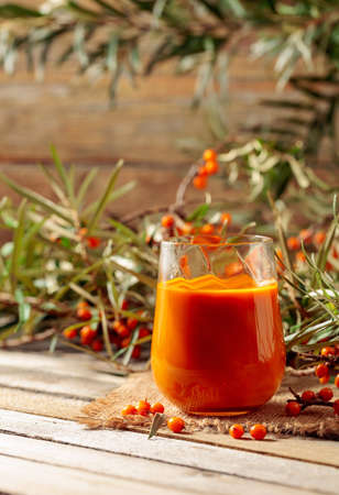 A glass of sea buckthorn juice with fresh berries on an old wooden table. Healthy and diet food....