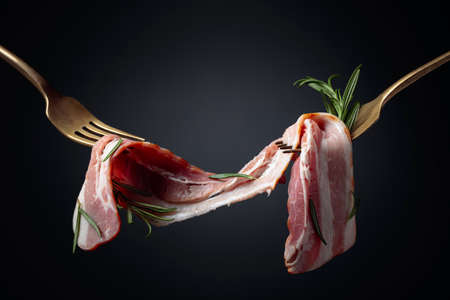 Bacon slices and rosemary on a fork. Smoked bacon on a black background.  Copy space.の写真素材