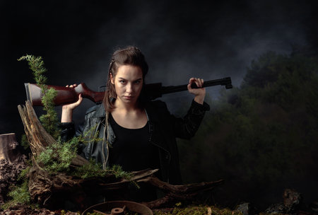 Portrait of a young woman with a rifle. A serious girl in a black leather jacket with a rifle looks...