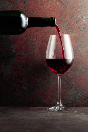 Red wine is poured from a bottle into a wine glass on rusty brown background. Frontal view with space for your text.の写真素材