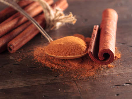 Cinnamon sticks and powder in a small spoon on an old wooden table.の写真素材