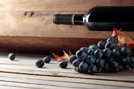 Bottle of red wine and a bunch of grapes on an old wooden table in the wine cellar. Selective focus.の写真素材