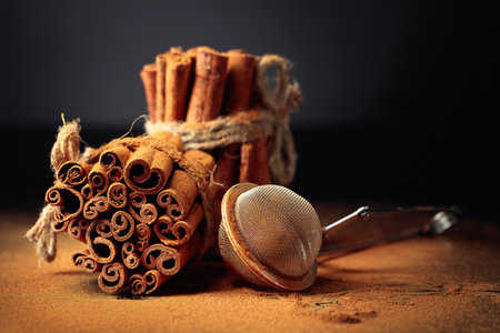 Ground cinnamon, cinnamon sticks, tied with jute rope on a black reflective background. Copy space.