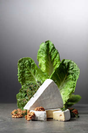 Fresh Brie cheese with lettuce, thyme, and walnuts on a grey stone table.の写真素材