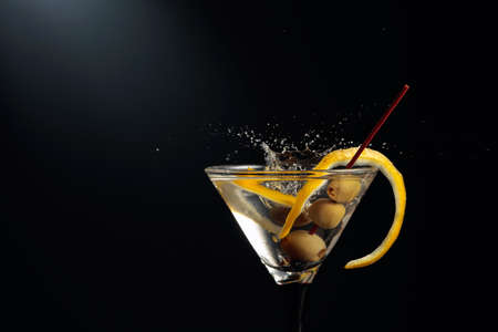 Green olive fall in glass with cocktail. Dry martini with lemon peel and green olives on a black...