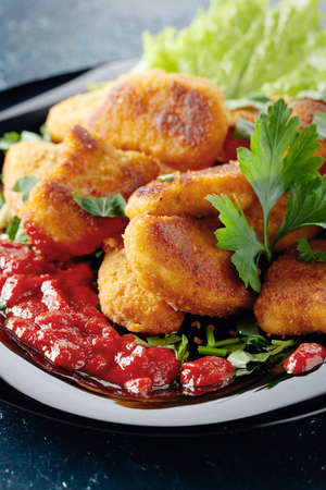 Fried chicken nuggets with ketchup, sprinkled with chopped parsley on a black plate.の写真素材