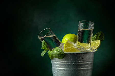 Wet glasses of strong alcoholic drink with lime and mint in a metal bucket with ice. Dark background with copy space.の写真素材