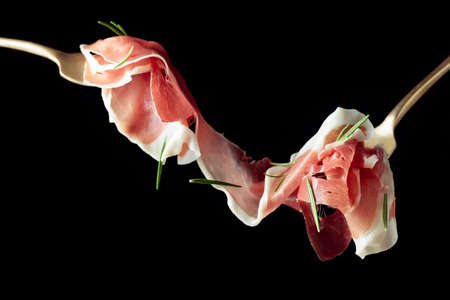 Sliced prosciutto with rosemary on forks, isolated on a black background.の写真素材