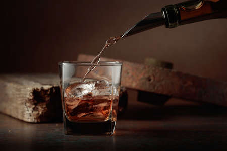 Whiskey is poured from a bottle into a frozen glass with natural ice. Rough rusty background.の写真素材