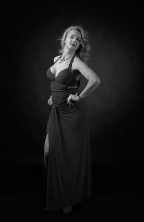 Attractive middle age woman in evening dress. Happy forty years blonde on a black background. Black and white.の写真素材