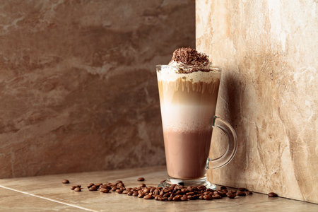 Milk coffee cocktail with whipped cream on a beige ceramic table. Copy space.