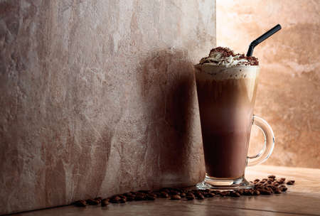 Milk coffee cocktail with whipped cream on a beige ceramic table with coffee beans. Copy space.の写真素材