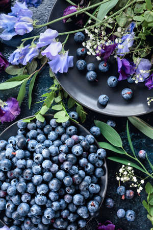 Fresh juicy blueberries on a black plate. Summer still life with blueberries, colored sweet peas and meadow grasses. View from the top.の写真素材