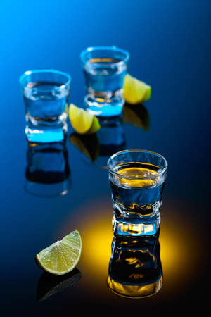 Tequila with lime slices on a black reflective background. Strong alcoholic drink in color bright lights.の写真素材