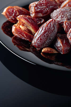 Dried sweet dates on a black plate, black reflective background.
