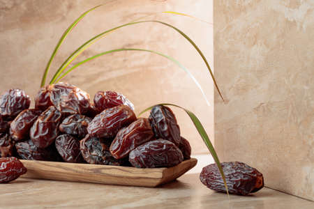 Fresh dates fruit in a wooden dish on a beige ceramic table.の写真素材