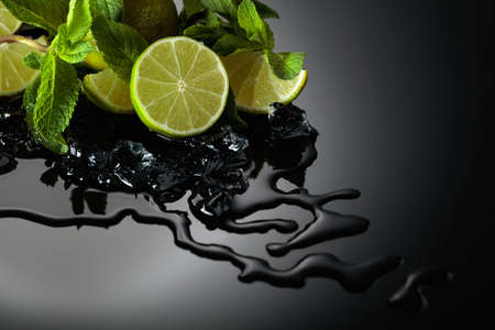 Slices of lime, mint leaves, and ice pieces on a wet black reflective background.の写真素材