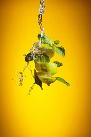 Fresh lime, mint, and ice in a splash on a yellow background.の写真素材