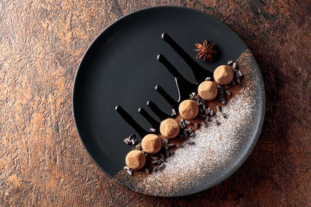 Chocolate truffles on a black plate with chocolate sauce. Sweets are sprinkled with cocoa powder and powdered sugar. Top view.の写真素材