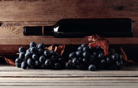 Bottle of red wine and a bunch of grapes on an old wooden table in the wine cellar. Selective focus.