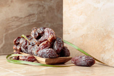 Fresh dates fruit in a wooden dish on a beige ceramic table.の写真素材