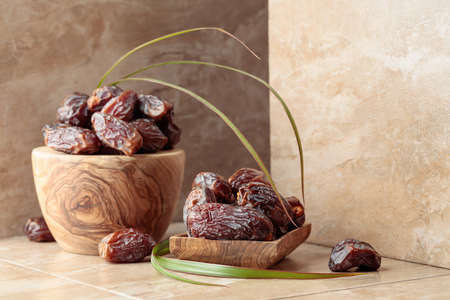 Fresh dates fruit in a wooden dish on a beige ceramic table.の写真素材