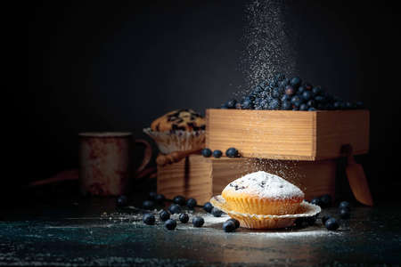 Blueberry muffins and berries in a wooden box. Muffins sprinkled with sugar powder. Copy space.の写真素材
