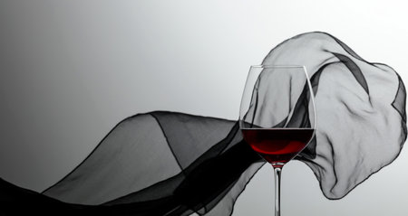 Glass of red wine on a background of waving black satin curtain.の写真素材