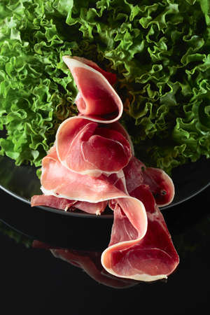 Prosciutto and fresh lettuce salad on a black reflective background.の写真素材