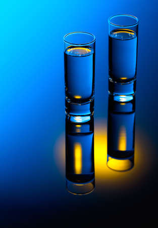 Vodka on a black reflective background. Strong alcoholic drink in color bright lights.の写真素材