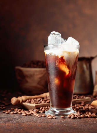 Ice coffee with cream in frozen glass and coffee beans on an old brown table with kitchen utensils. Copy space.の写真素材