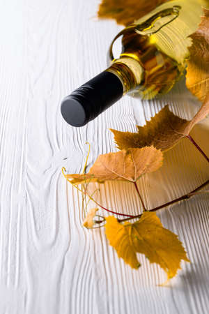 An unopened bottle of white wine and grapevine on an old wooden background. Wine on a white table. Copy space.の写真素材