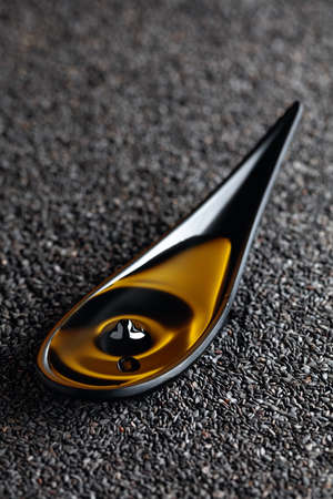 Sesame oil and raw black sesame seeds. A drop of oil fall in a small black dish.の写真素材