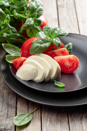 Mozzarella with tomatoes and basil on an old wooden table.の写真素材