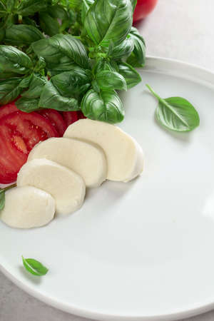 Fresh mozzarella with red tomatoes and green basil on a white plate.の写真素材