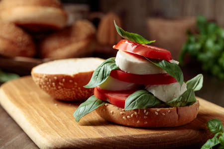 Sandwich with mozzarella, tomatoes, and basil on an old wooden table.の写真素材