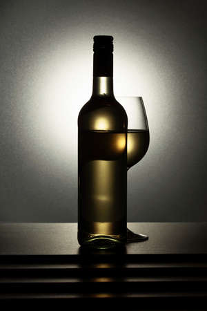 Bottle and glass of white wine on a black table.の写真素材