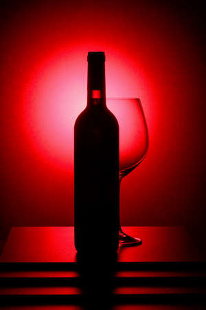 Bottle of red wine and an empty glass. Red backlight.の写真素材