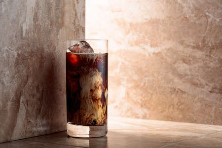 Iced coffee with cream on a beige ceramic table. Copy space.