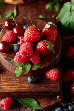 Assorted fresh berries with leaves. Strawberries, raspberries blueberries, and sweet cherries on an old vintage table.の写真素材