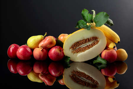 Fresh fruits on a black reflective background. Apples, bananas, melon, pears, and peaches are presented.の写真素材
