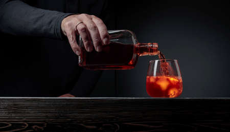 Bartender pouring whiskey into glass at bar counter. Alcoholic drink pouring from a bottle into a frosted glass with ice. Copy space.の写真素材