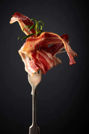 Slices of fried bacon garnished with rosemary on a black background.の写真素材