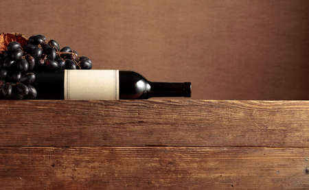 Bottle of red wine and grapes on a old wooden table. On a bottle old empty label.の写真素材