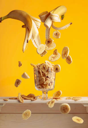 Banana chips in a glass bowl on a yellow background.の写真素材