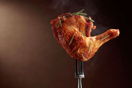 Hot grilled chicken leg sprinkled with rosemary on a brown background. Chicken drumstick on a fork. Copy space.の写真素材