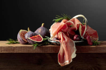 Prosciutto with figs, rosemary, and red olives on a old wooden table. Copy space.