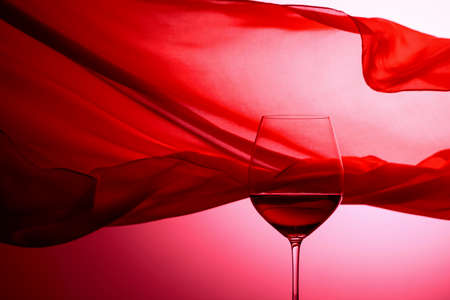 Glass of red wine on a background of waving red satin curtain.の写真素材