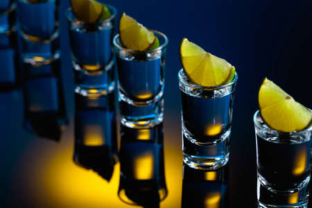 Tequila with lime slices on a black reflective background. Strong alcoholic drink in color bright lights. Selective focus.の写真素材